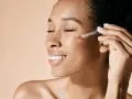 Kobieta aplikuje serum z witaminą E na twarz, dbając o zdrową skórę.