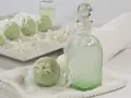 Zielone kule do kąpieli i buteleczka z płynem, ozdobione białymi kwiatami. Idealne na relaksującą kąpiel, wiesz, na co.