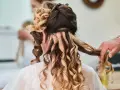 Fryzury na wesele średnie włosy: loki i doczepiane pasma tworzą objętość i blask. Stylista dopracowuje detale.