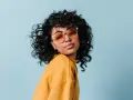Dziewczyna z burzą loków, w okularach i żółtym swetrze, prezentuje efekt metody curly girl.