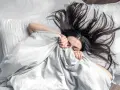 Kobieta z rozpuszczonymi, ciemnymi włosami śpi pod jasną kołdrą. Jej twarz jest częściowo ukryta, a ręce trzymają materiał.
