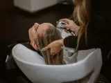 Relaks w salonie fryzjerskim: delikatne mycie włosów odżywką. Woda spływa po głowie, a dłonie fryzjerki czule pielęgnują pasma.