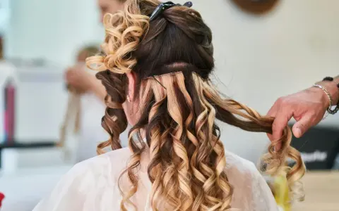 Fryzury na wesele średnie włosy: loki i doczepiane pasma tworzą objętość i blask. Stylista dopracowuje detale.