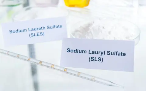 Biały proszek z etykietą "Sodium Lauryl Sulfate (SLS)" obok pipety laboratoryjnej.