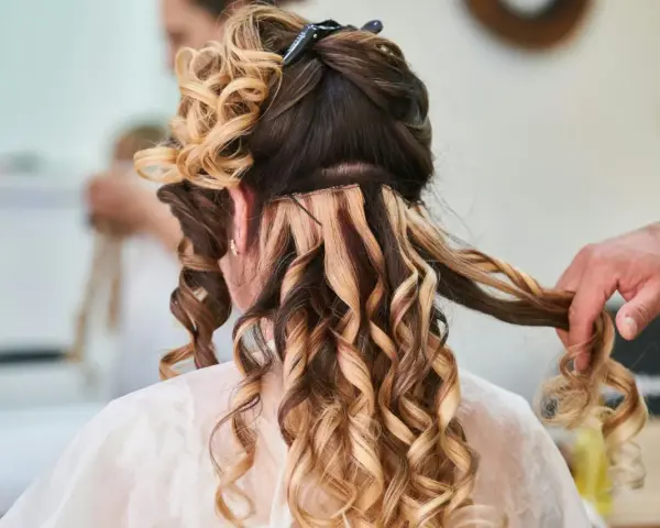 Fryzury na wesele średnie włosy: loki i doczepiane pasma tworzą objętość i blask. Stylista dopracowuje detale.