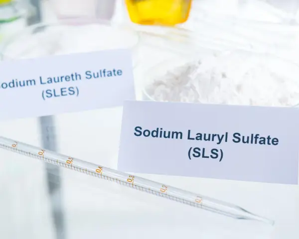 Biały proszek z etykietą "Sodium Lauryl Sulfate (SLS)" obok pipety laboratoryjnej.