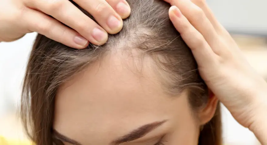 Kobieta sprawdza swoje włosy przy linii czoła, szukając sposobów, jak pozbyć się baby hair i uzyskać gładką fryzurę.