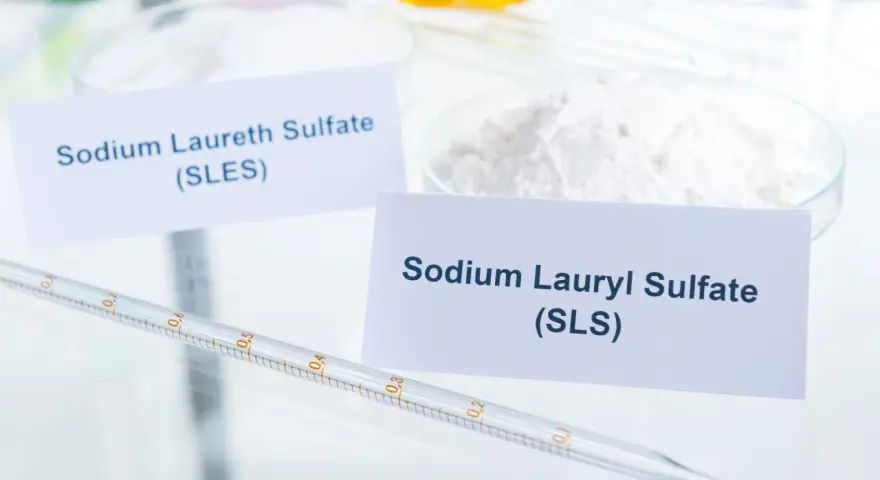 Biały proszek z etykietą "Sodium Lauryl Sulfate (SLS)" obok pipety laboratoryjnej.