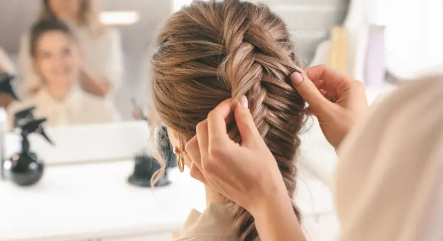 Stylistka tworzy dobierane warkocze. Warkocz rybi ogon jest w trakcie zaplatania, tworząc elegancką fryzurę.