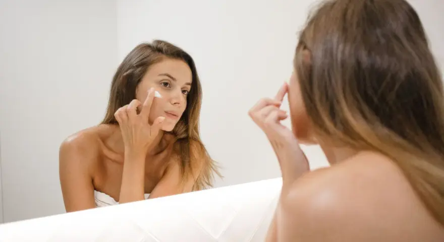 Kobieta nakłada krem na twarz, zastanawiając się, jak działa retinol. Skóra staje się gładsza i młodsza.