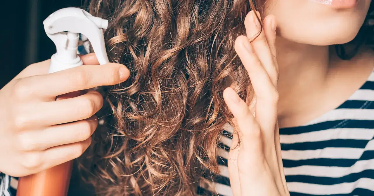 Kobieta spryskuje swoje kręcone włosy, stosując metodę curly girl.