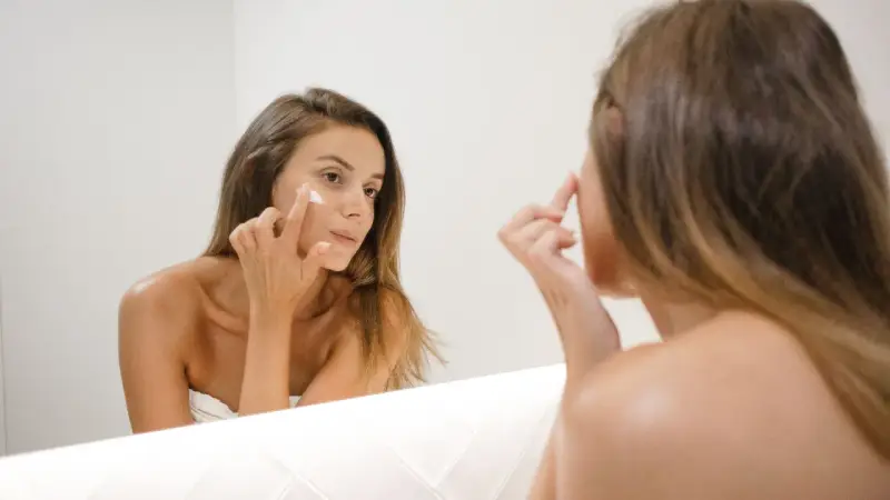 Kobieta nakłada krem na twarz, zastanawiając się, jak działa retinol. Skóra staje się gładsza i młodsza.